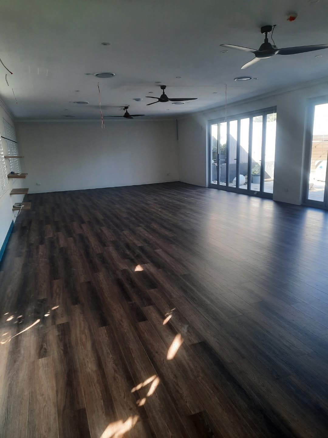 Large open common area after vinyl plank installation with ceiling fans and bi-fold glass doors