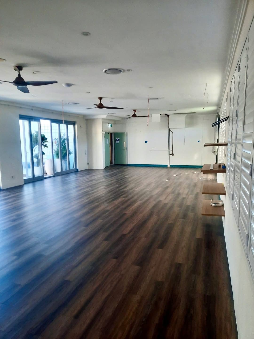 Wide angle of hostel lounge with dark vinyl plank flooring and glass sliding doors