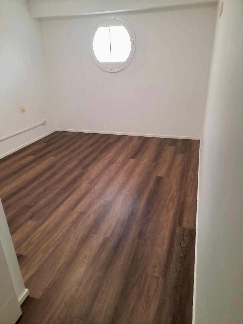 Small guest pod with round porthole window and dark vinyl plank flooring