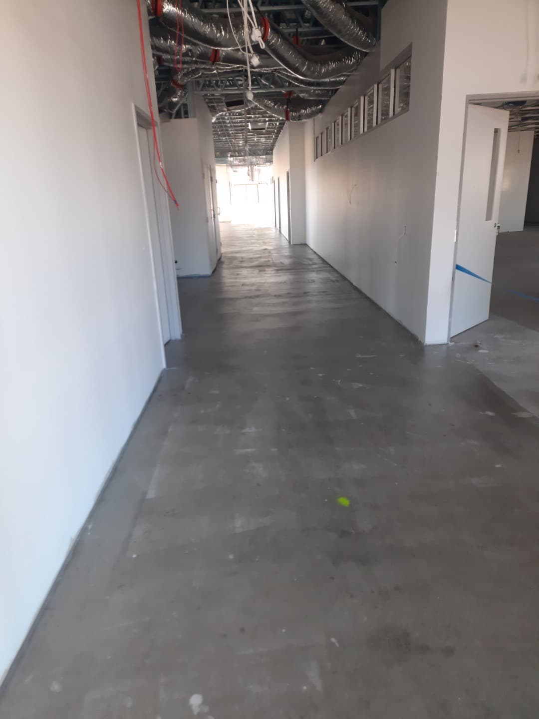 Wide gallery corridor showing concrete subfloor length of building with exposed services overhead