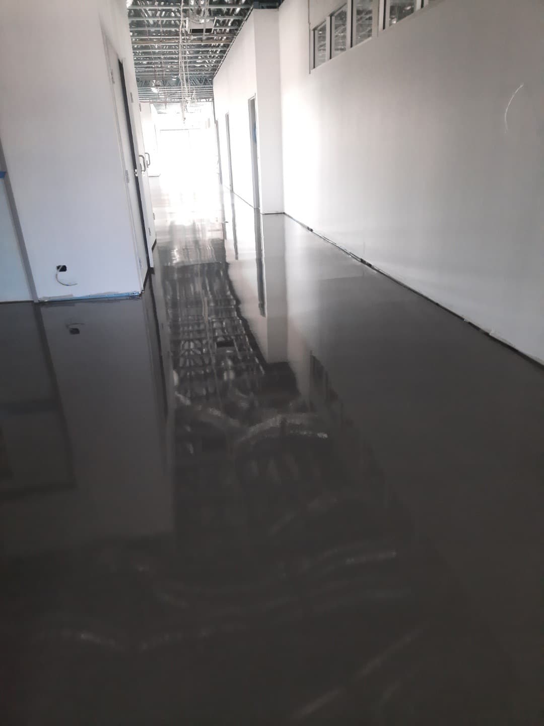 Main corridor with freshly applied self-levelling compound — highly reflective wet surface