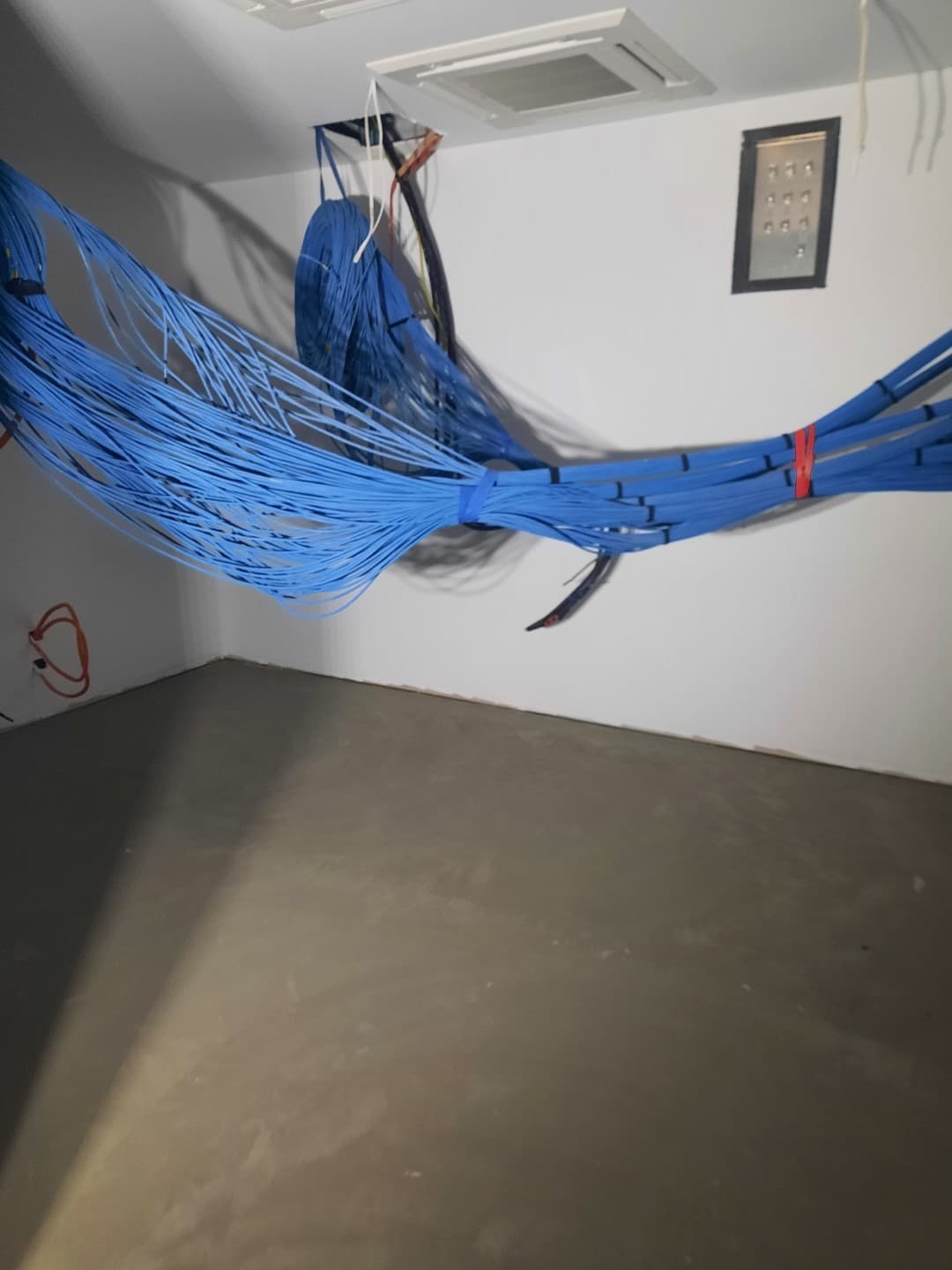 Room with raw concrete subfloor and large bundles of blue data cabling awaiting connection