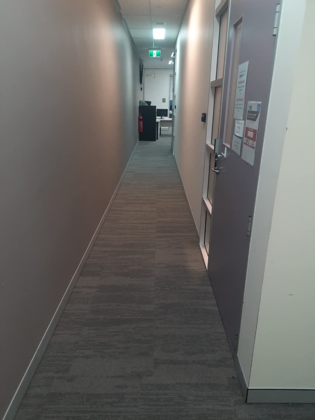 Long office corridor with charcoal carpet tiles, fire extinguisher and exit signage visible