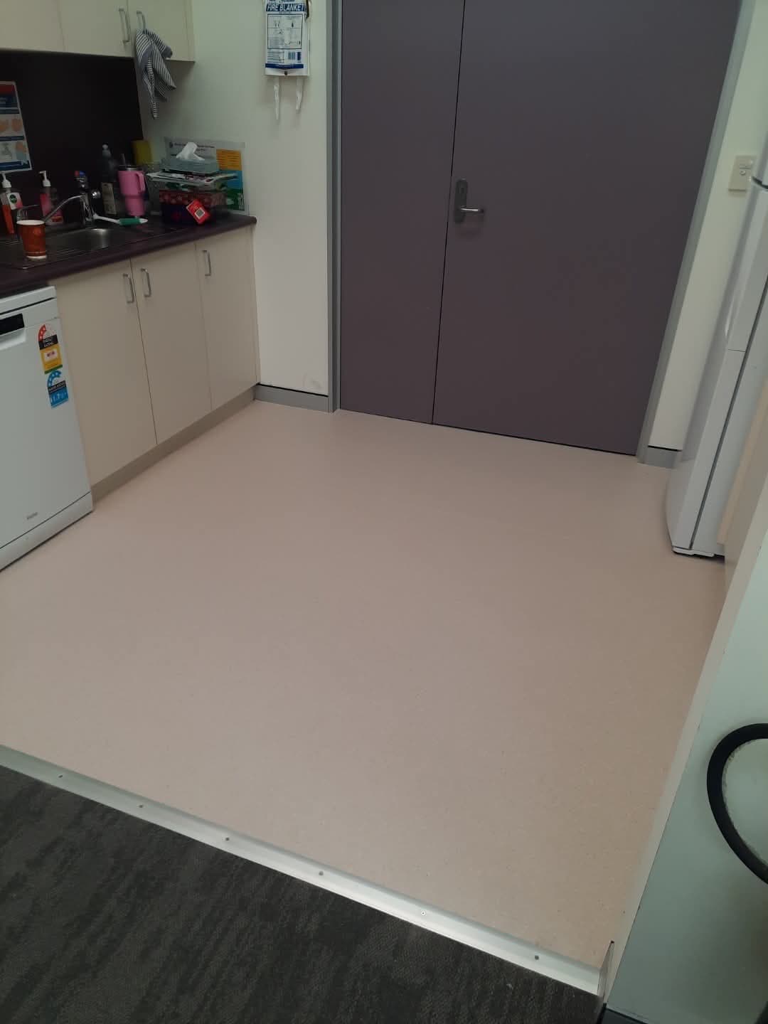 Kitchen and breakroom with light beige sheet vinyl flooring transitioning to carpet at the threshold