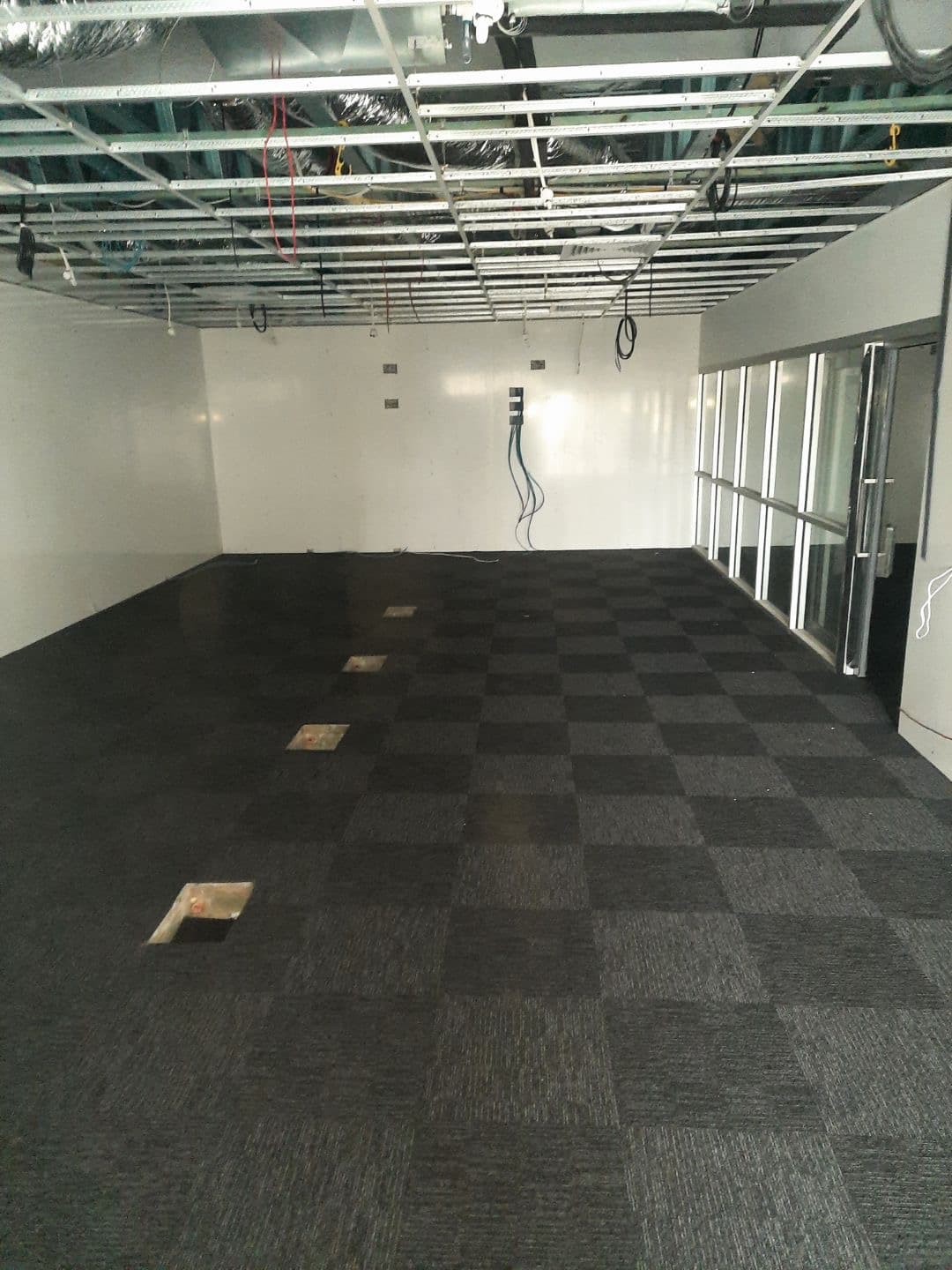 Dark charcoal carpet tiles being installed in the open-plan area with floor box cutouts