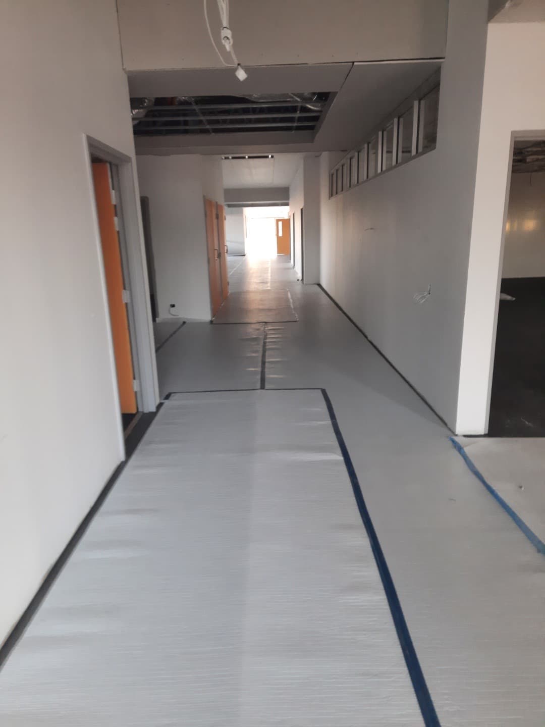 LVT installation in progress — grey tiles being laid through a long corridor with blue seam tape