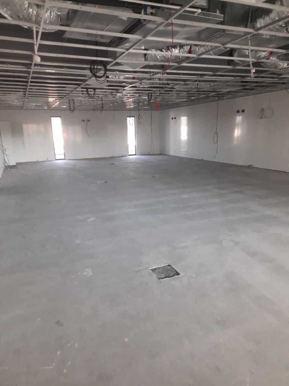 Large room with concrete screed prepared before flooring installation, exposed ceiling grid above