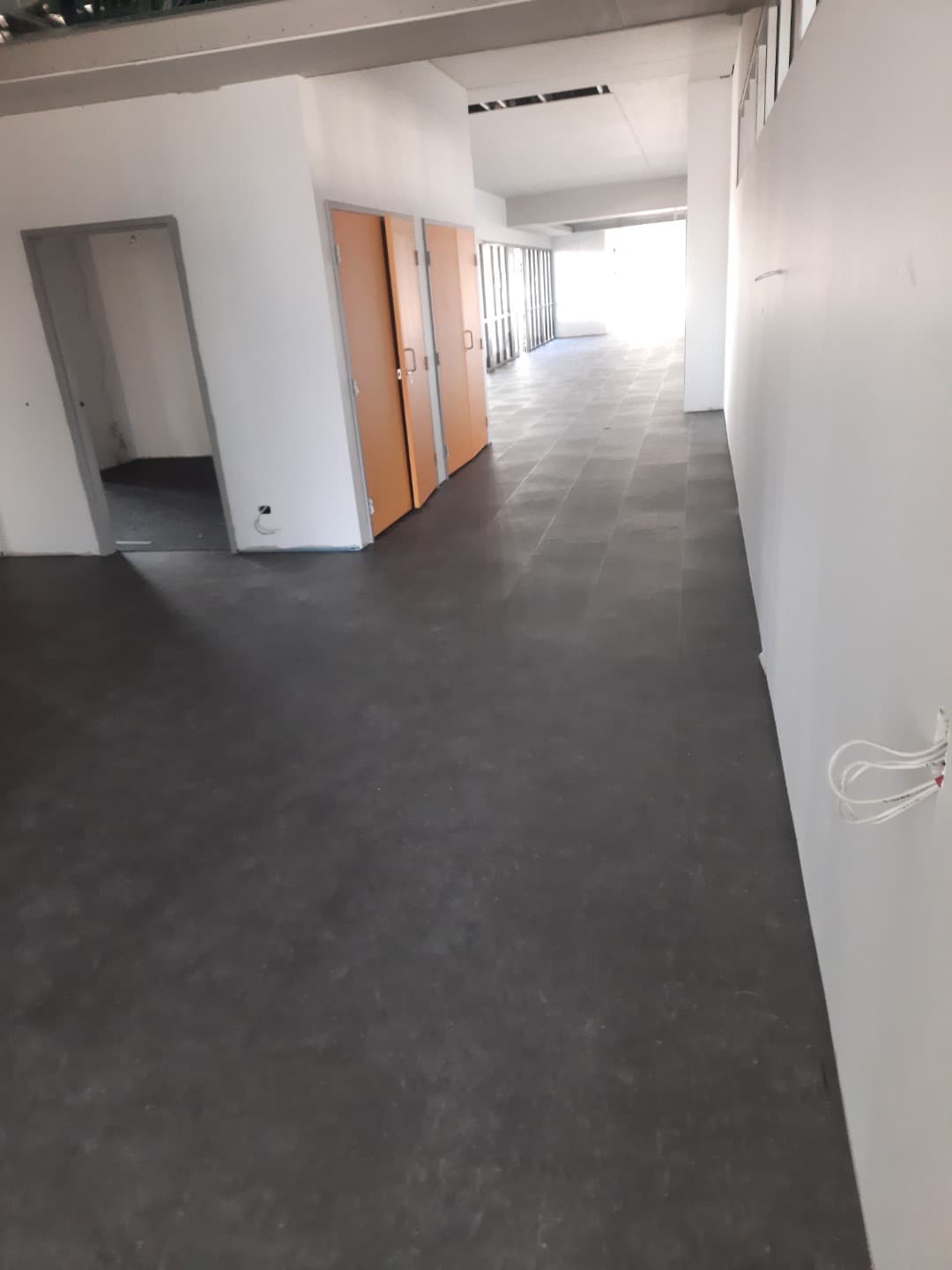 Long main corridor with completed dark grey LVT flooring and orange-doored rooms along the wall