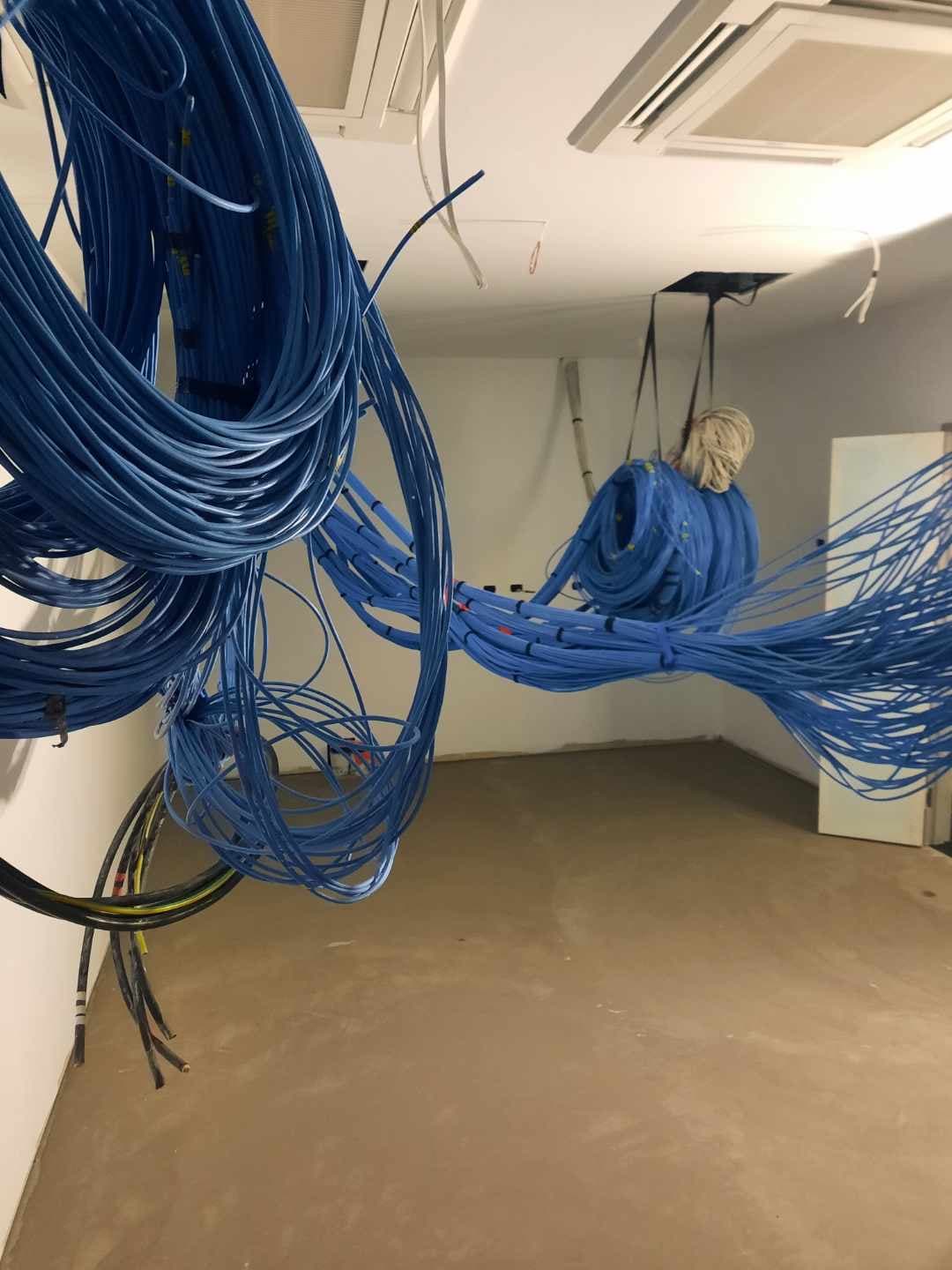 Office area before installation — bare concrete subfloor with blue data cabling suspended from ceiling frame