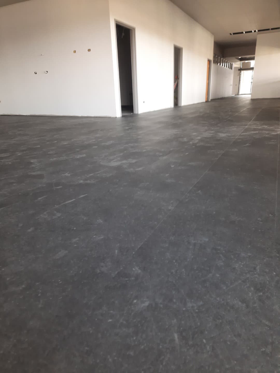 Large open area with dark grey LVT flooring completed, looking toward the entry
