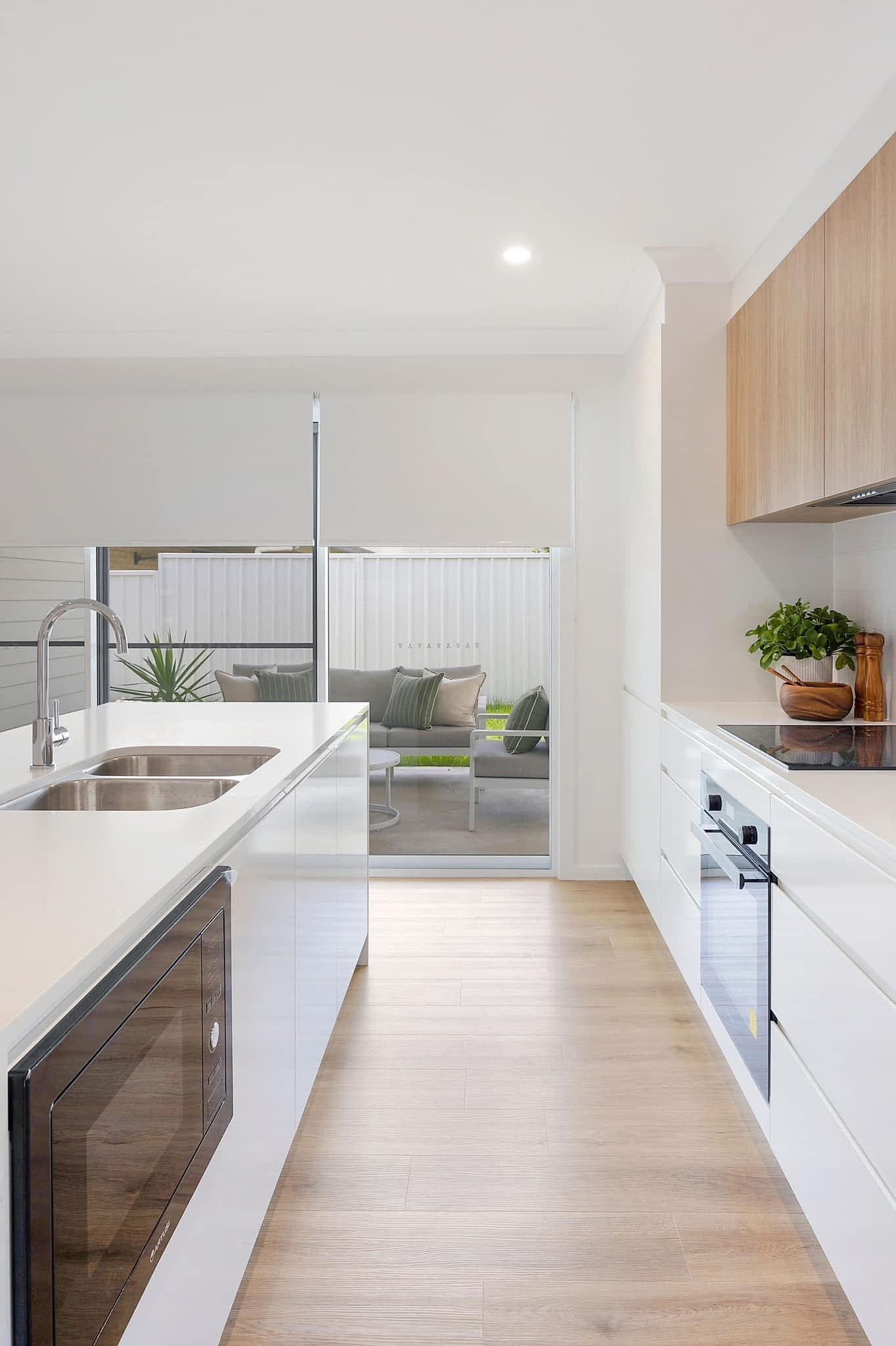 Modern white kitchen with light vinyl plank flooring and sliding door opening to alfresco area