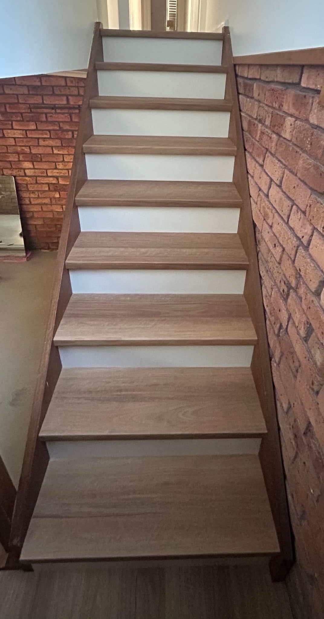 Completed staircase with light oak vinyl plank treads and white risers against exposed brick wall — Hamilton