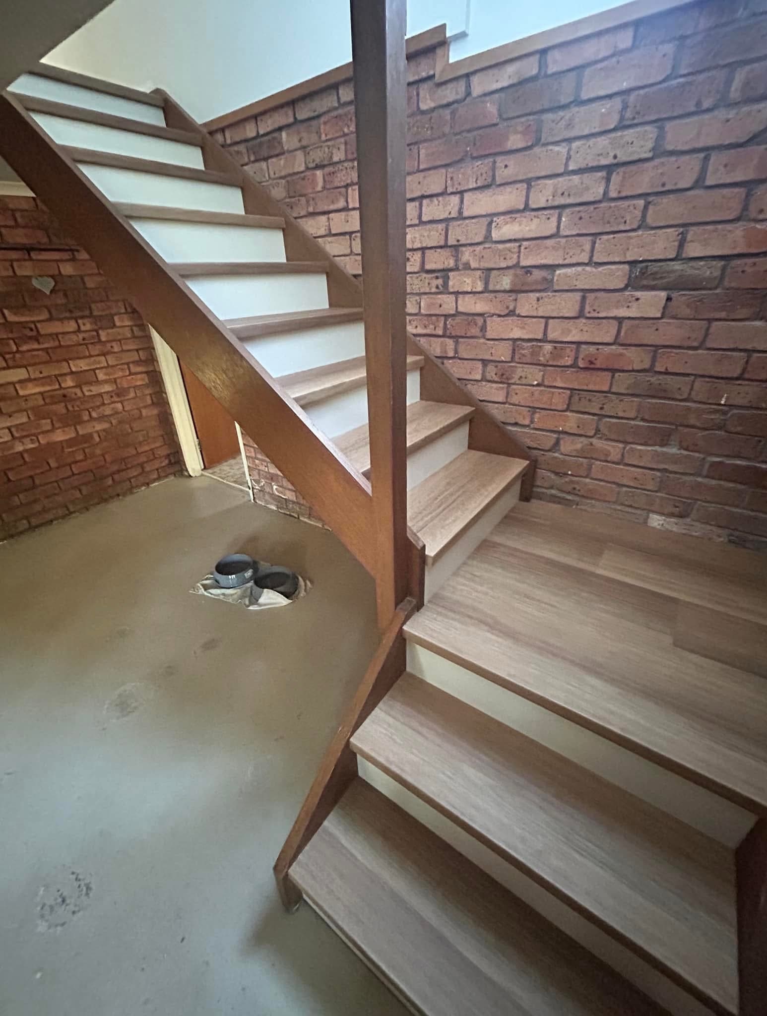 Wide view of renovated staircase with vinyl plank treads, white risers and exposed brick