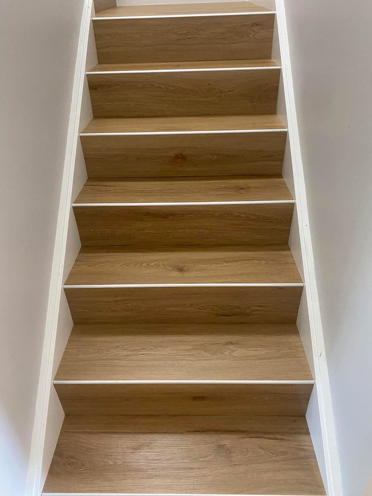Close-up of staircase looking up, showing warm oak vinyl plank fitted to every tread with white painted risers — Mayfield