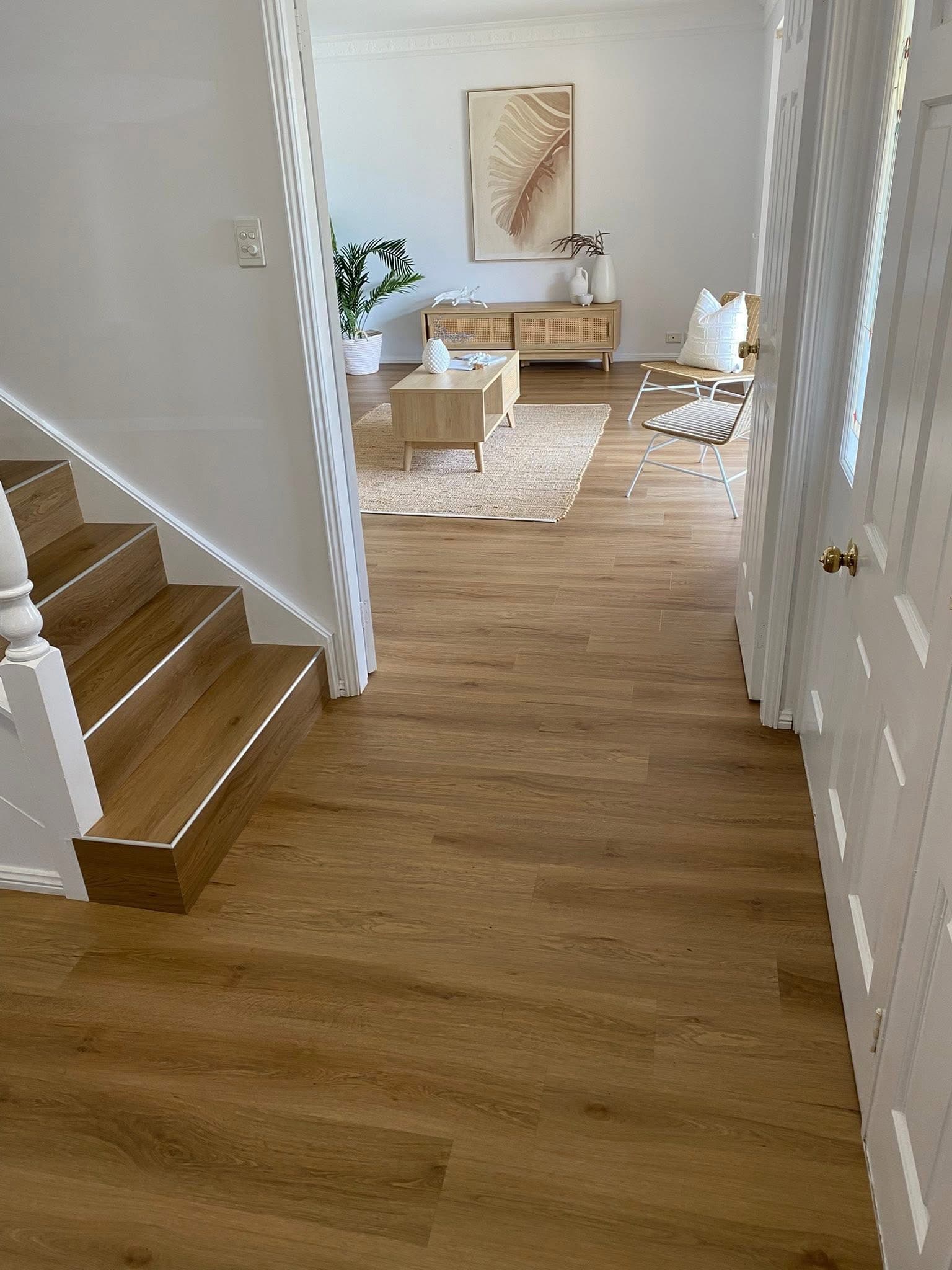 Entry hallway with warm vinyl plank flooring, renovated stairs to the left and lounge visible ahead