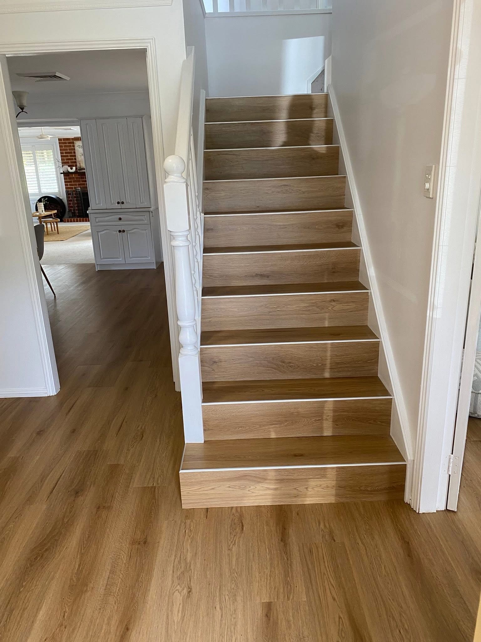 Renovated staircase with warm honey oak vinyl plank treads and white risers, looking up from entry hallway — Toronto NSW