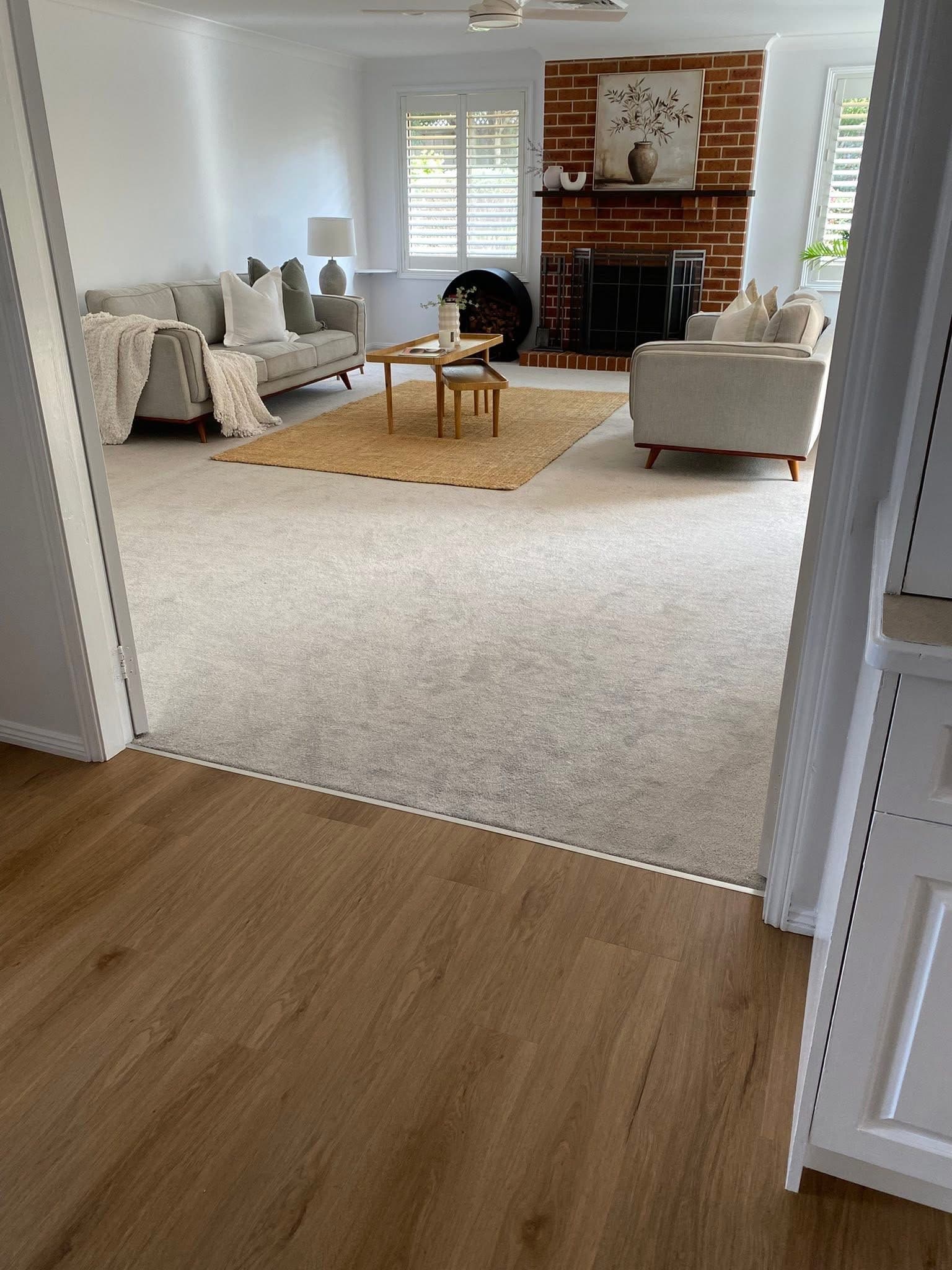 Transition from vinyl plank hallway to new light grey carpet in the lounge room with exposed brick fireplace