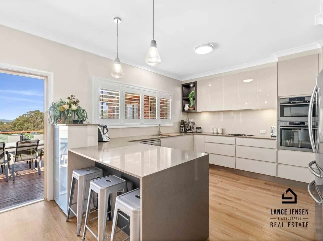 Modern kitchen with island bench and warm vinyl plank flooring opening to outdoor deck